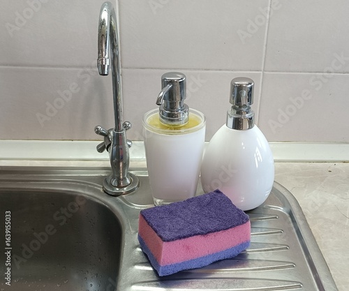 Kitchen Sink Accessories. Dish Soap and Sponge.
​Cleaning Supplies on a Sink. Modern Kitchen Sink.