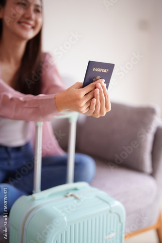 Asian adult woman prepares for international journey holding passport ready to embark on exciting travel adventure with luggage at home