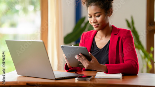 Young African American Woman Working on Tablet and Laptop in Home Office Red Blazer Business Casual Attire Remote Work Digital Device Technology