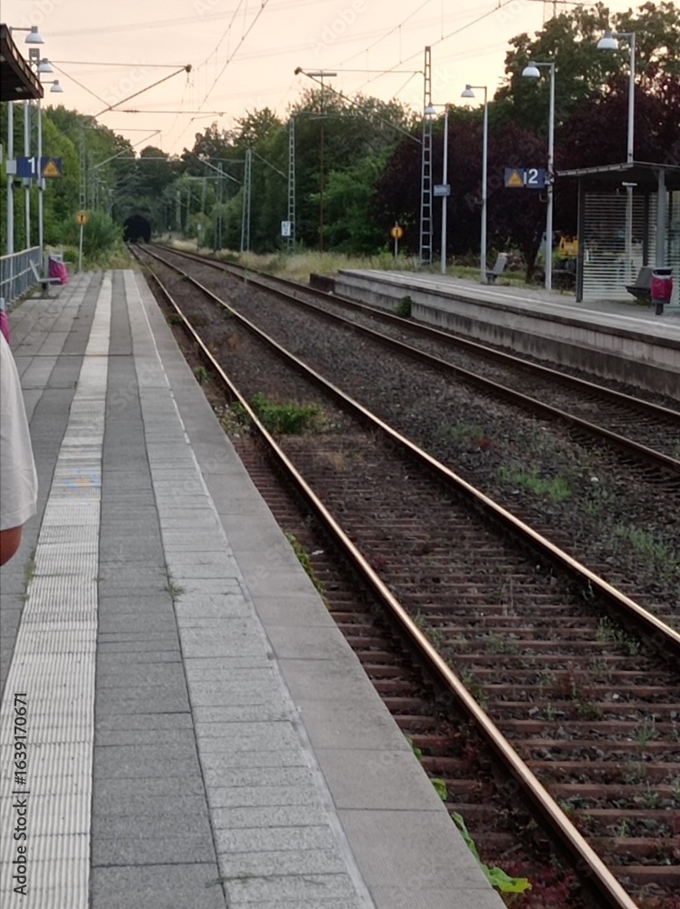 Naklejka premium Gerade Bahngleise neben einem leeren Bahnsteig unter leicht bewölktem Himmel – ruhige Verkehrsszene im Regionalverkehr.