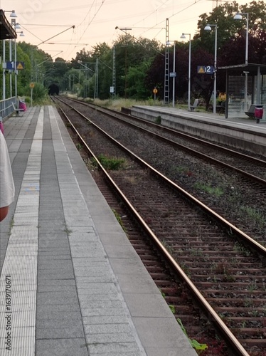 Gerade Bahngleise neben einem leeren Bahnsteig unter leicht bewölktem Himmel – ruhige Verkehrsszene im Regionalverkehr.