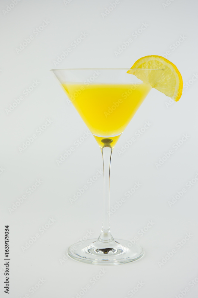 An orange cocktail in a classic martinin glass with a wedge of lemon set against a white background. An orange cocktail in a classic martinin glass with a wedge of lemon set against a white background.