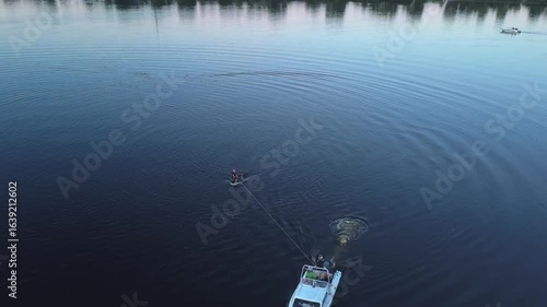 The athlete gets up from the water on foilboarding holding on to the rope tied to the boat in the evening aerial view