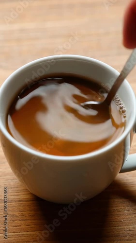 Spoon stirs tea inside a ceramic mug on a wooden tabletop  
