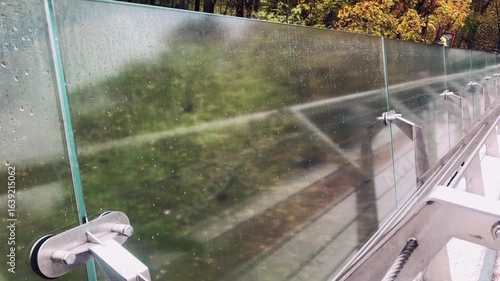 Steel railings with glass bridge, after rain in autumn, reflection of passing people.