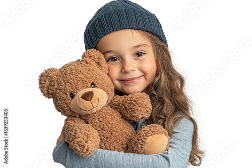 Happy little girl hugging a soft teddy bear while wearing a cozy beanie indoors during a playful winter day