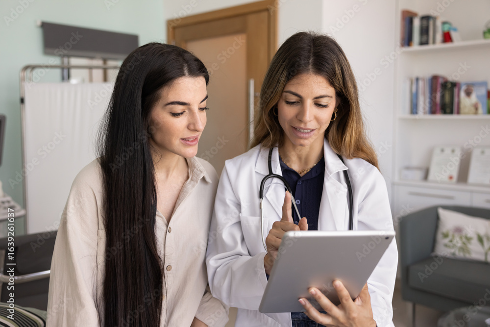 Positive female Hispanic doctor showing medical test result on tablet to woman, using gadget for consultation of patient, explaining prescription, treatment, diagnosis, checkup electronic report Positive female Hispanic doctor showing medical test result on tablet to woman, using gadget for consultation of patient, explaining prescription, treatment, diagnosis, checkup electronic report