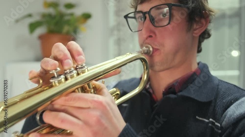 Close-up of a man playing trumpet indoors with puffed cheeks and focused expression. Moment of musical concentration and expression captured in warm indoor lighting.