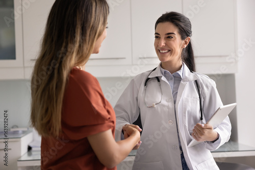 Fotografia Cheerful young Latin practitioner woman shaking hands with female patient, congr
