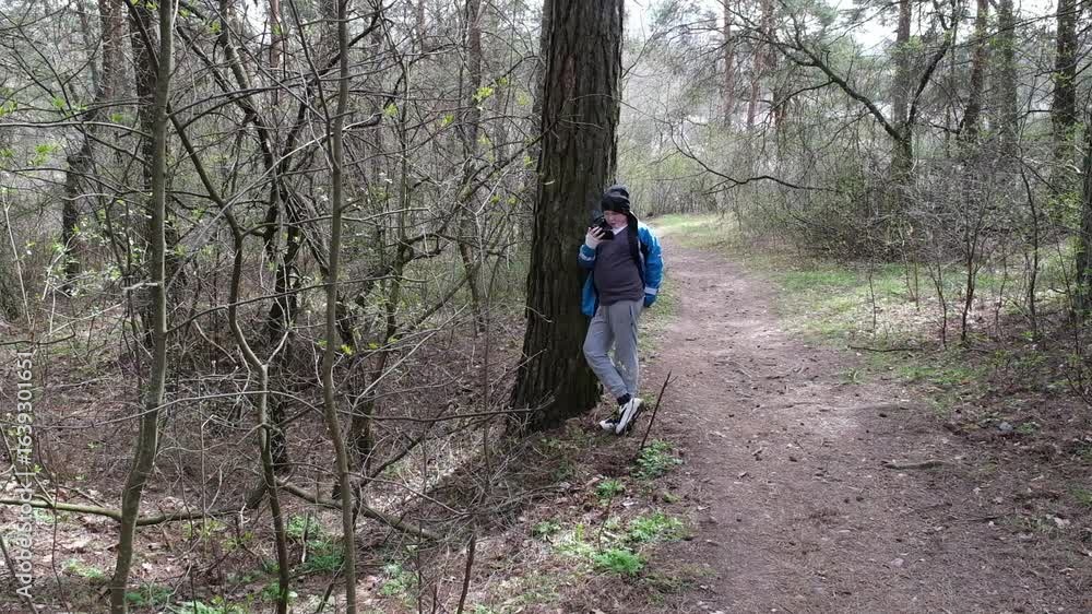 A boy dressed in casual outdoor clothing walks along a dirt path in a green spring forest, holding a smartphone. A boy dressed in casual outdoor clothing walks along a dirt path in a green spring forest, holding a smartphone.