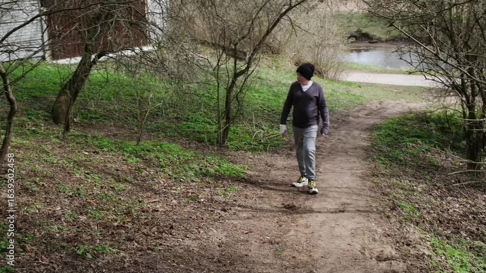 A boy dressed in casual outdoor clothing walks along a dirt path in a green spring forest, holding a smartphone. A boy dressed in casual outdoor clothing walks along a dirt path in a green spring forest, holding a smartphone.