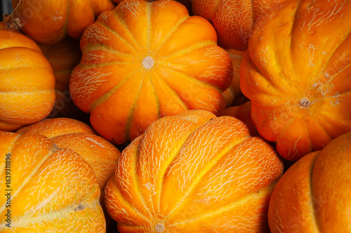 A pile of bright yellow orange ribbed melons with prominent white veining. These unique textures and shapes make the image ideal for autumn harvest, organic farming, or rustic market visuals