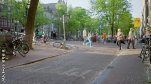 Wallpaper Mural Urban street scene in amsterdam with blurred pedestrians and bicycles, showcasing vibrant city life under leafy trees and sunlit paths in the netherlands. Torontodigital.ca