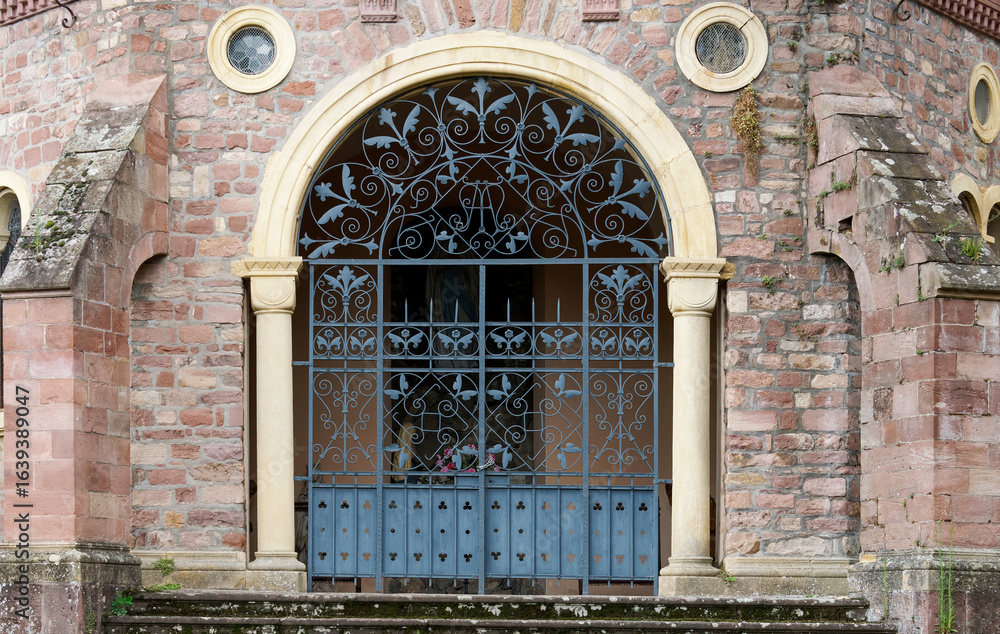 Obraz premium Historic Ornamental Iron Gate with Arched Entry and Stonework Design