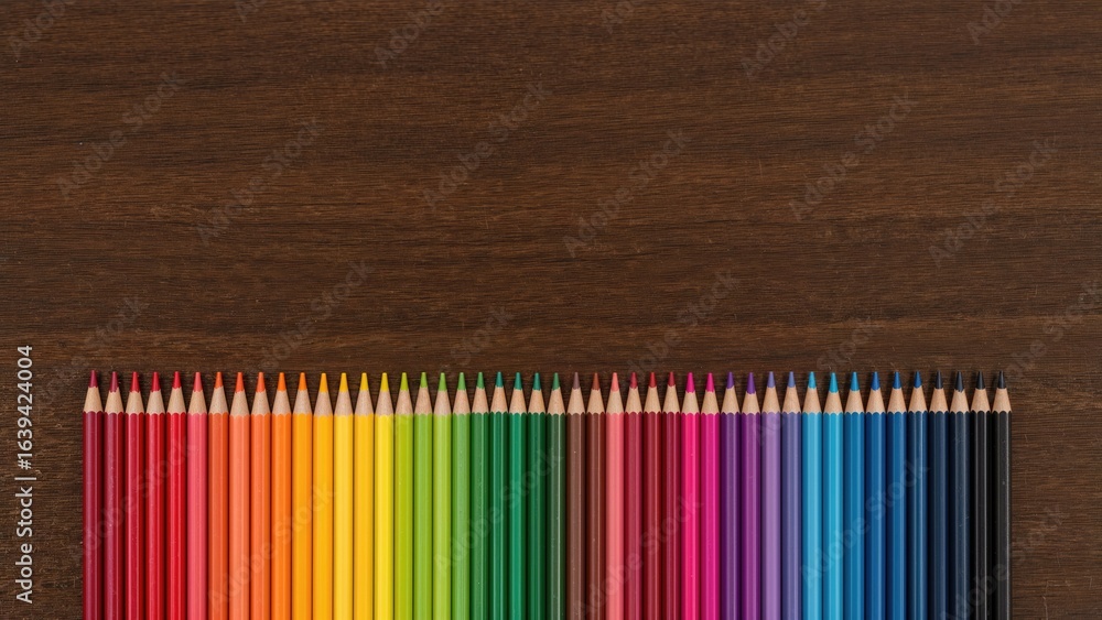 Obraz premium Wooden surface with colored pencils arranged to form a colorful rainbow