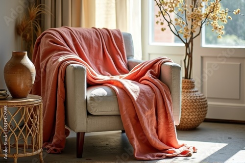 Cozy armchair with coral blanket and decorative vases in sunlit living room