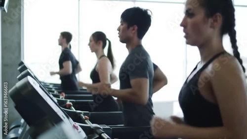 People of varying ages and fitness levels exercise on treadmills in a bright, modern gym setting, promoting health and wellness.