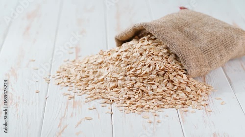 dry rolled oats or rolled oat in sack on a light kitchen table. Raw oat flakes are scattered out of the bag. Sack of oat flakes spill.