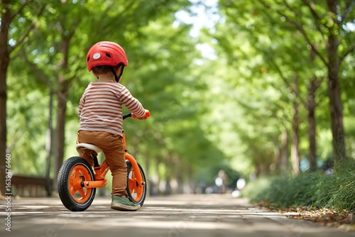 Child in red helmet riding orange bike in green, sunny park.
