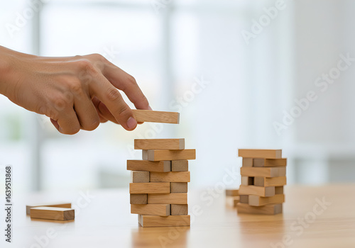 Hand placing a wooden block on a tower. A person carefully builds a tower, representing business strategy, risk management, and planning. The concept illustrates growth, fragile foundations, and skill