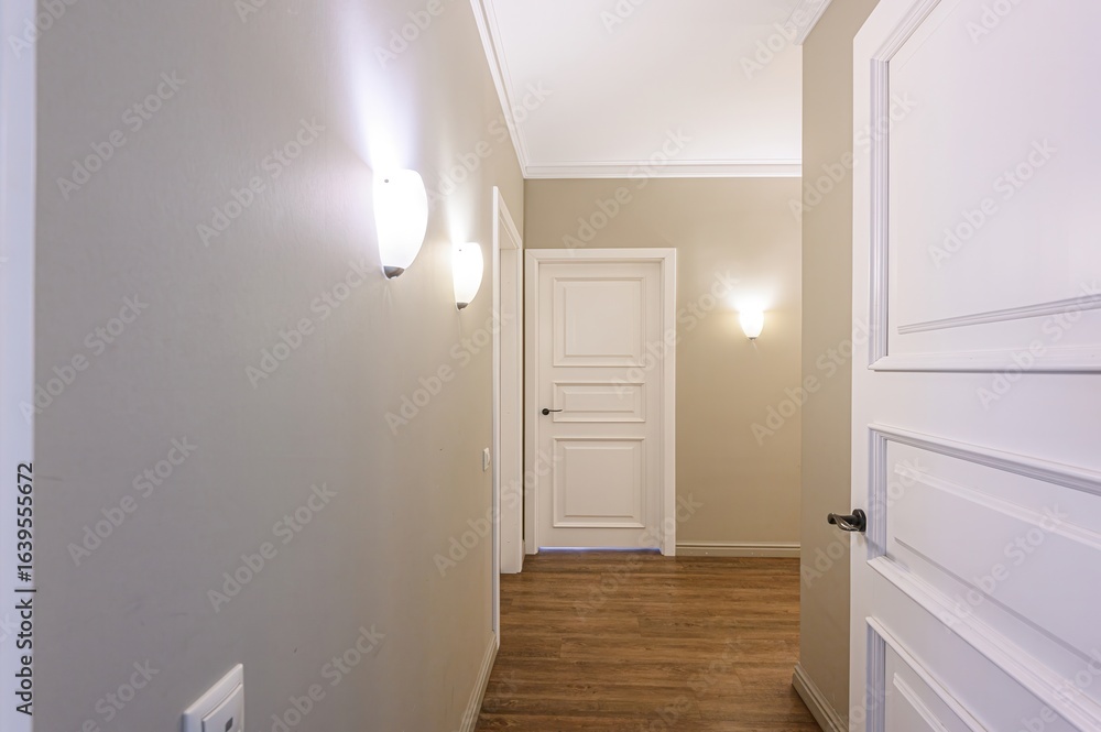 Fototapeta premium Hallway with white doors, wall lamps, and wooden floors. Neutral color scheme