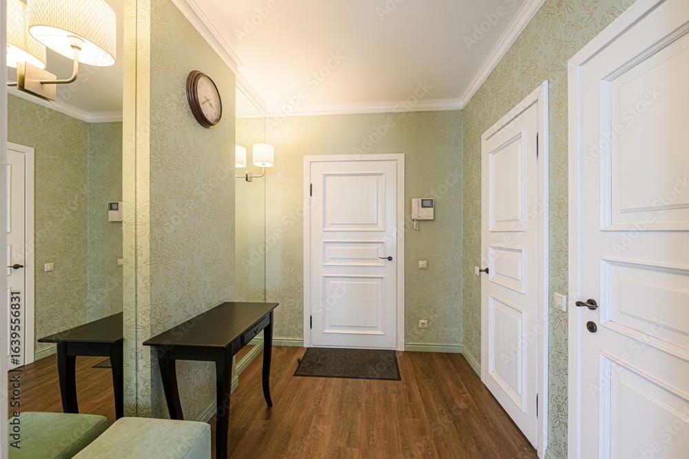 Fototapeta premium cozy hallway featuring floral wallpaper, wooden floors, and white doors. A dark console table sits against a mirrored wall