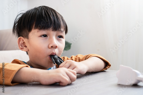 Asian boy is seen putting a toy in his mouth, sucking and chewing on  it as part of natural toddler behavior