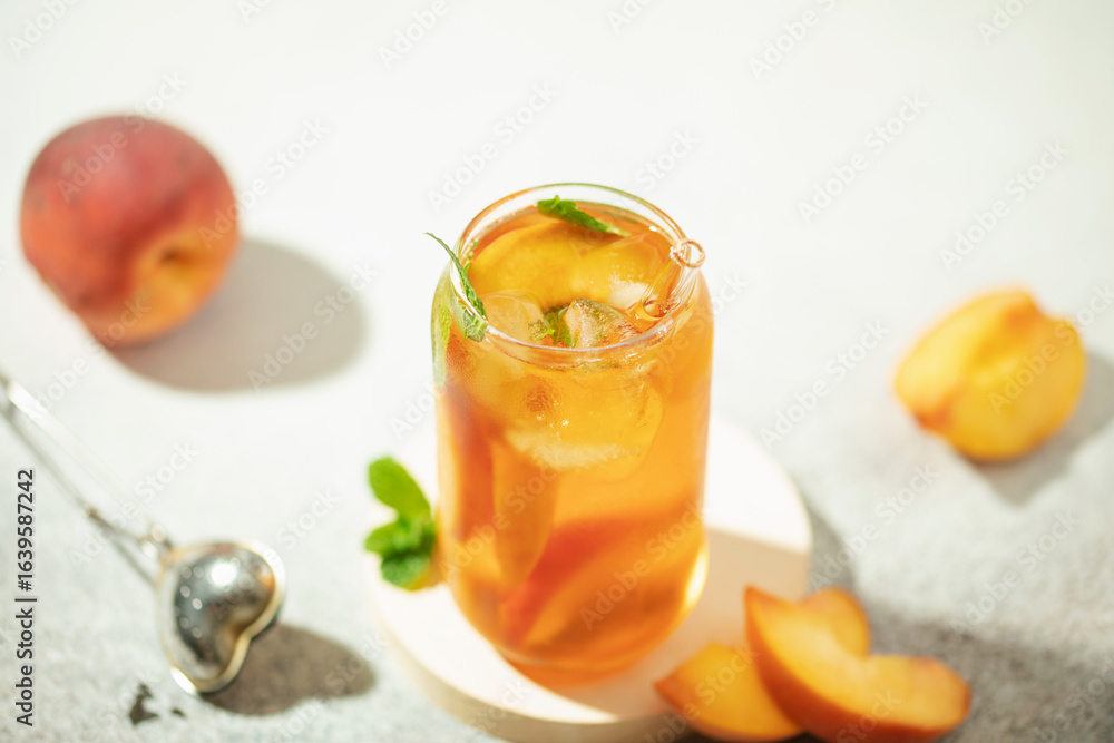 Fototapeta premium Fruit iced tea with peaches and apples in a glass on the table. Summer drink concept