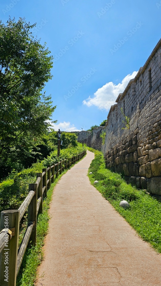Fototapeta premium Sunny Path Along Historic Stone Fortress Wall, 성곽길과 여름 하늘