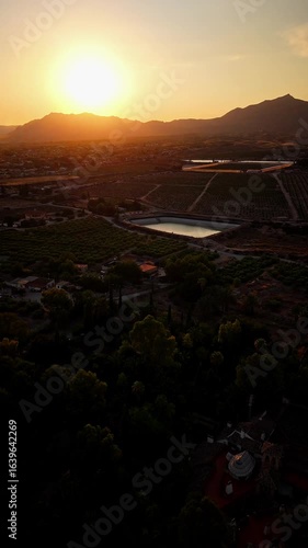 Drone video captures golden hour sunlight over agricultural fields, reservoirs, and distant mountains, creating a warm and peaceful rural scene in Spain.