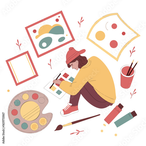 Young artist sitting on the floor surrounded by art supplies and colorful abstract paintings creating a new masterpiece