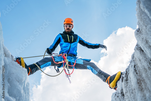 Fotografi Climber in vibrant gear overcomes over crevasse on icy glacier during Lenin peak ascent under clear sky with snow-covered peaks in background