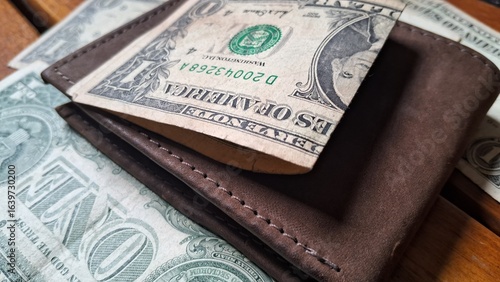 Dollar bill on top of leather wallet on wooden background