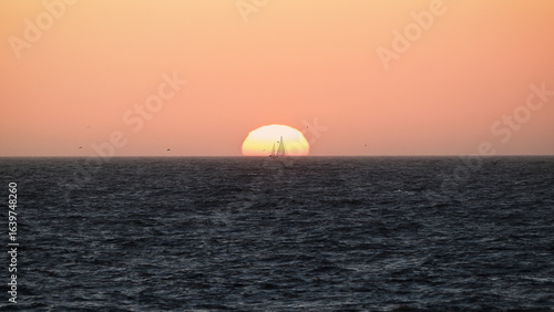 Silhouette of a sailboat against the backdrop of the setting sun over the sea