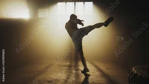 Foto Muscular athlete performing a powerful high kick in a hazy gym
