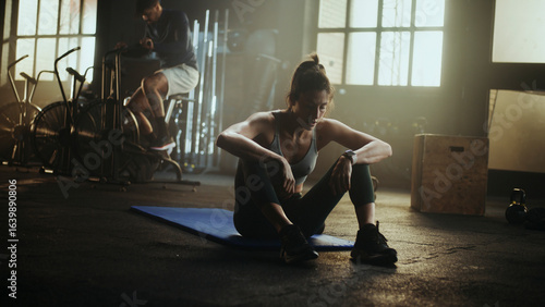 Foto Tired sportswoman resting after training in gym with man cycling in background