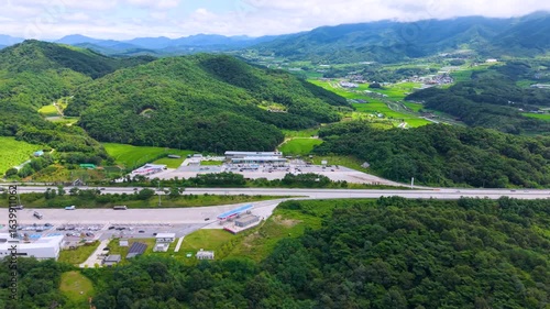 Aerial Drone View of Highway and Cars Driving Through Green Fields and Forest, with Vast Summer Landscape, Blue Sky, and Clouds for a Healing Scenery