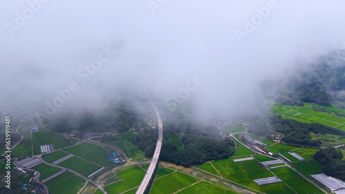 Aerial Drone View of Highway and Cars Driving Through Green Fields and Forest, with Vast Summer Landscape, Blue Sky, and Clouds for a Healing Scenery