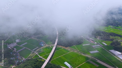 Aerial Drone View of Highway and Cars Driving Through Green Fields and Forest, with Vast Summer Landscape, Blue Sky, and Clouds for a Healing Scenery