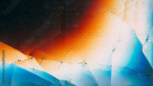 Fractured monitor. Crashed glass. Blue white orange spectrum colorful light glow on cracked black background abstract blur free space.
