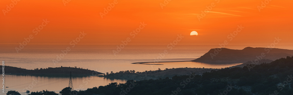 Fototapeta premium Beautiful sunset over the sea with islands and hills silhouette creating a peaceful and breathtaking scenery