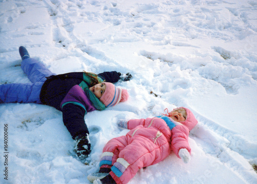 Children in the 80s, playing in the snow, making snow angels, wearing a snowsuit. Vintage scan, may have imperfections