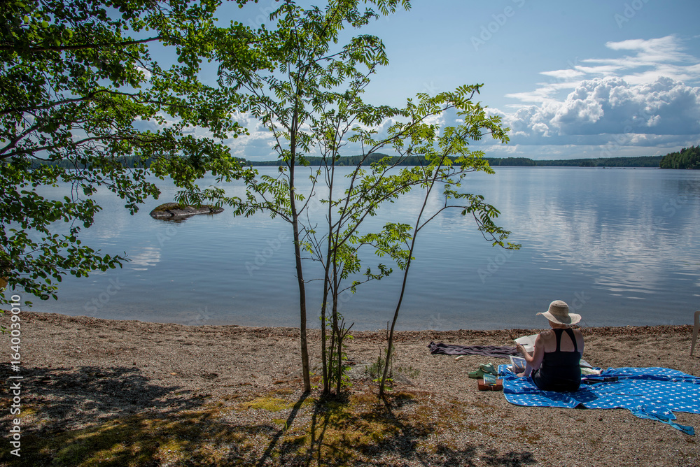 Fototapeta premium Woman sitting on the beach at Lake Saimaa in Finland