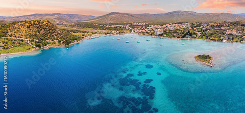 Fototapeta Naklejka Na Ścianę i Meble -  Amazing sunset seascape with boats floating on calm crystal clear turquoise water near coastline with green hills and mountains in the background