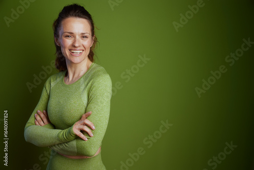 Tableau sur toile A cheerful woman in green athletic wear stands with arms crossed, promoting fitness, health, and a positive attitude against a light green studio backdrop