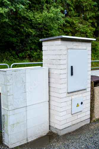 Outdoor electrical distribution cabinet and utility connection box mounted on a brick pillar next to a street, in a rural residential area.