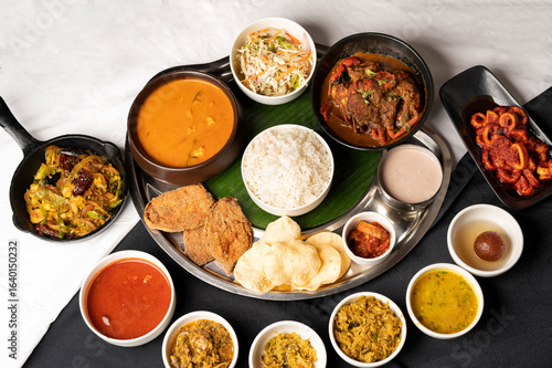 Top view of Goan fish thali with rawa fried kingfish, crab, calamari, prawns, fish curry, sambar, rice, papad, dal, thrissur, sol curry, gulab jamun, served with copper bottle on black and white cloth