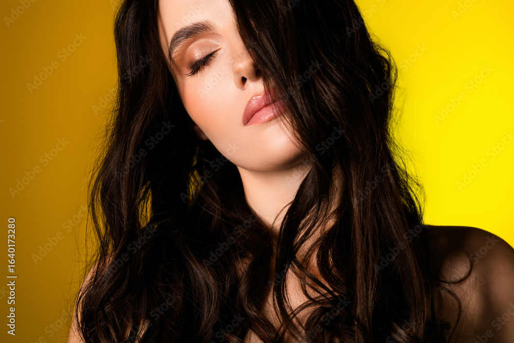 Naklejka premium Charming young woman with brunette hair and glamorous makeup posing against yellow background