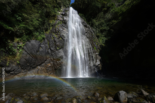 Serene Waterfall Cascading into Emerald Pool with Rainbow, Lush Green Foliage, Dramatic Rock Face.