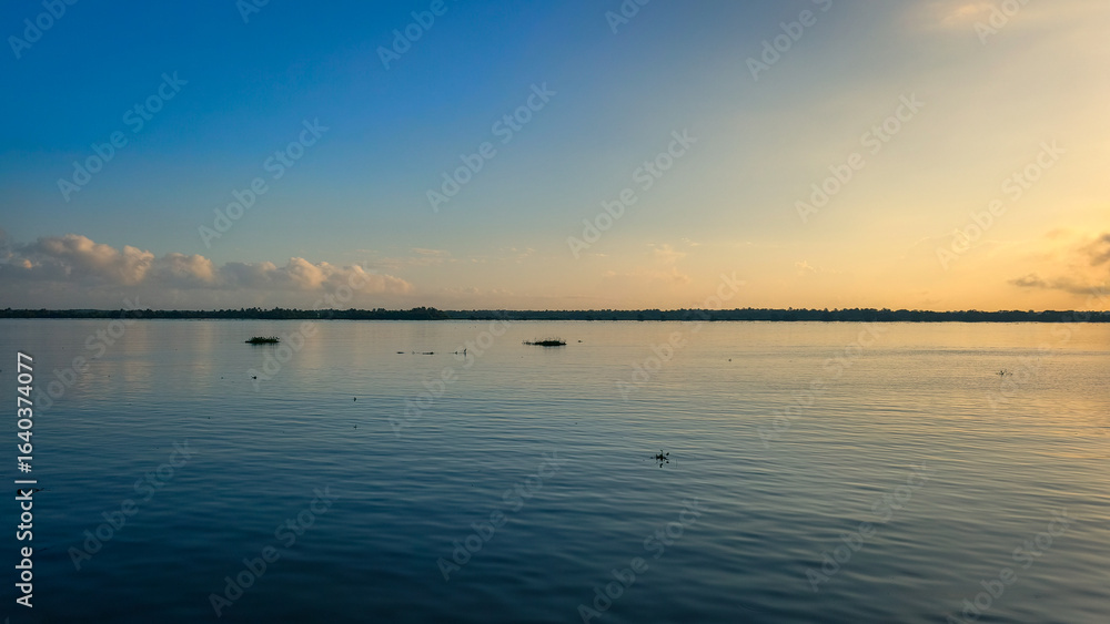 Naklejka premium Expansive blue skies reflecting off the calm waters of the Magdalena River at dusk. Clouds add depth and contrast, creating a breathtaking view of nature's beauty in Colombia
